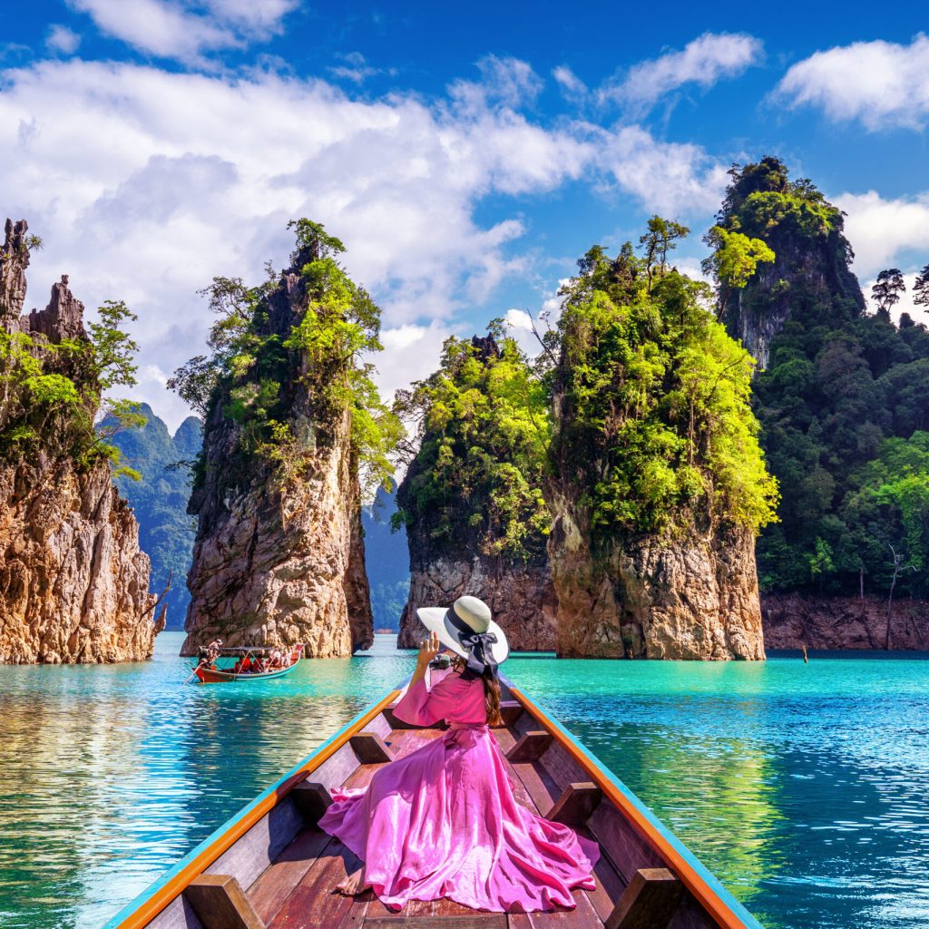 Beautiful girl sitting on the boat and looking to mountains in Ratchaprapha Dam at Khao Sok National Park, Surat Thani Province, Thailand.